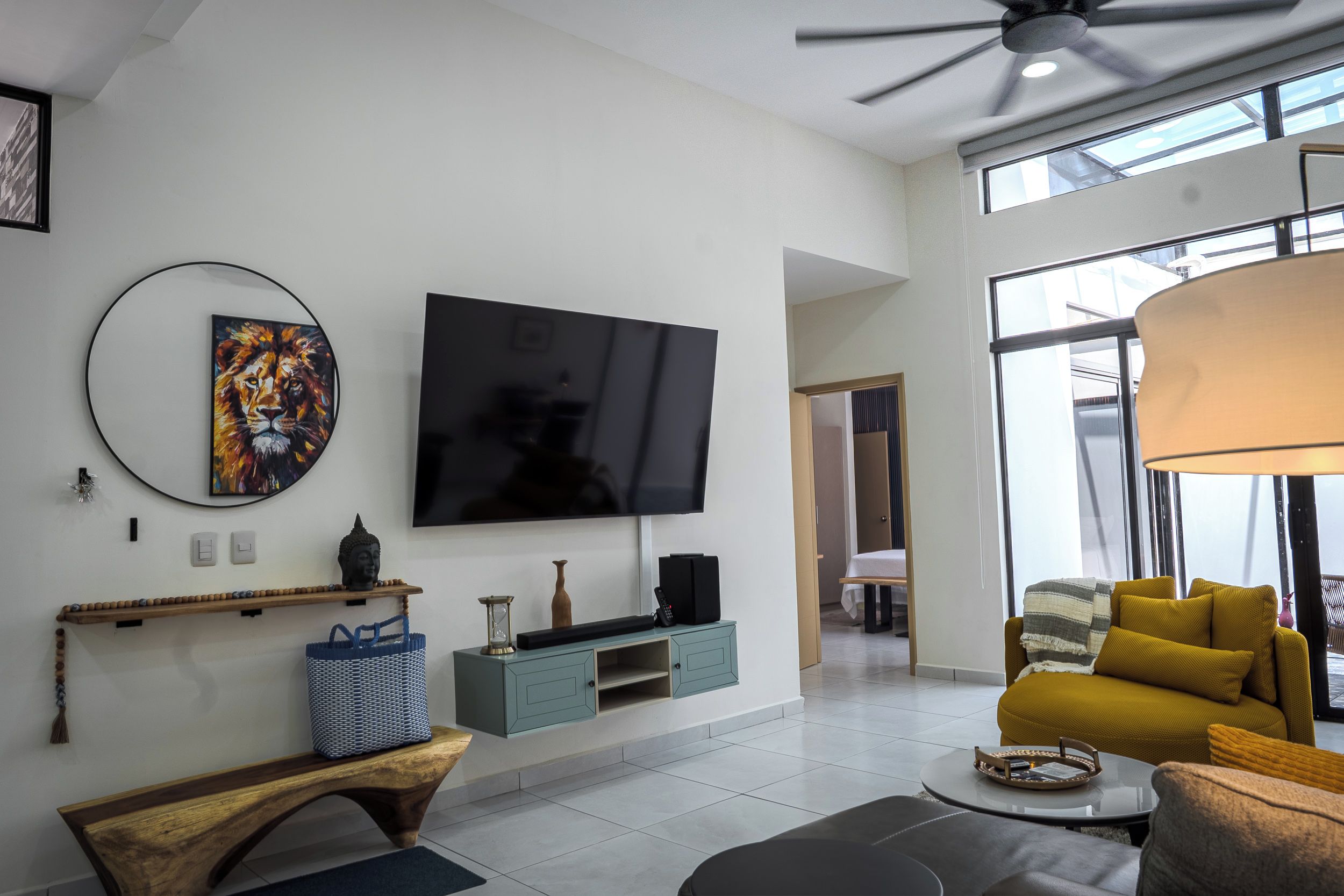 A modern living room with a flat-screen TV, a Buddha statue, a woven basket, and a yellow sofa.