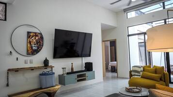A modern living room with a flat-screen TV, a Buddha statue, a woven basket, and a yellow sofa.