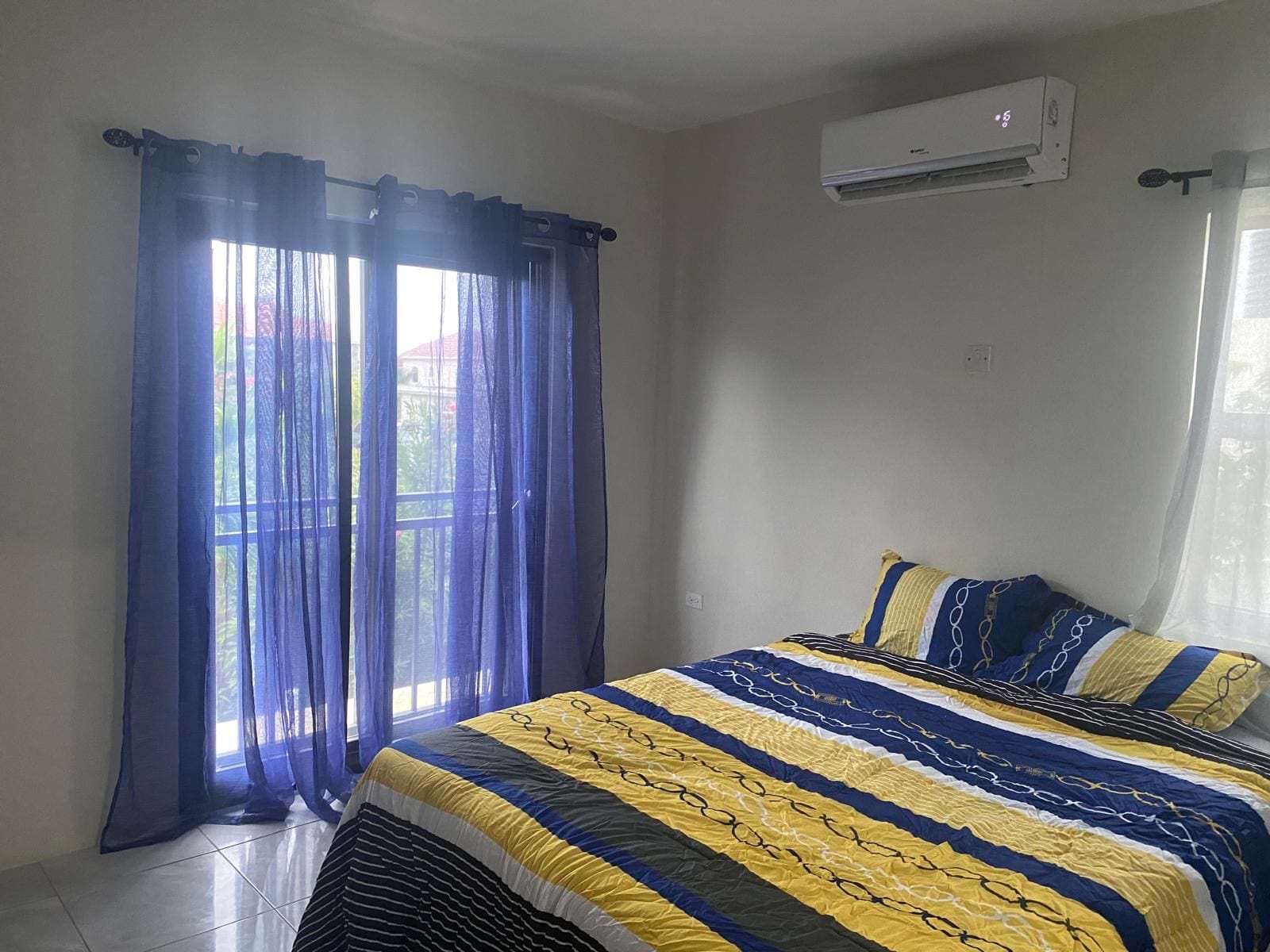 A bedroom with a bed, curtains, an air conditioning unit, and a window.