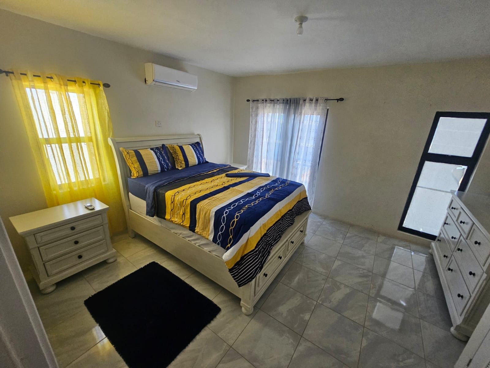 A bedroom with a bed, nightstand, dresser, and an air conditioning unit.