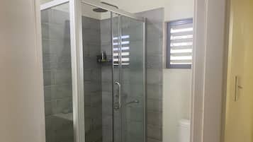 Box de chuveiro com vidro, chuveiro, vaso sanitário e janela com persianas.