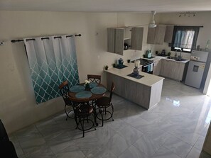 A modern kitchen with a central island, a dining area with a round table and chairs, and a patterned curtain. - Beautiful 2-bedroom house with AC in Discovery Bay (Discovery Bay)