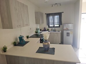 Una cocina moderna con una isla central, armarios empotrados, un ventanal con cortina y un refrigerador con una etiqueta de advertencia.