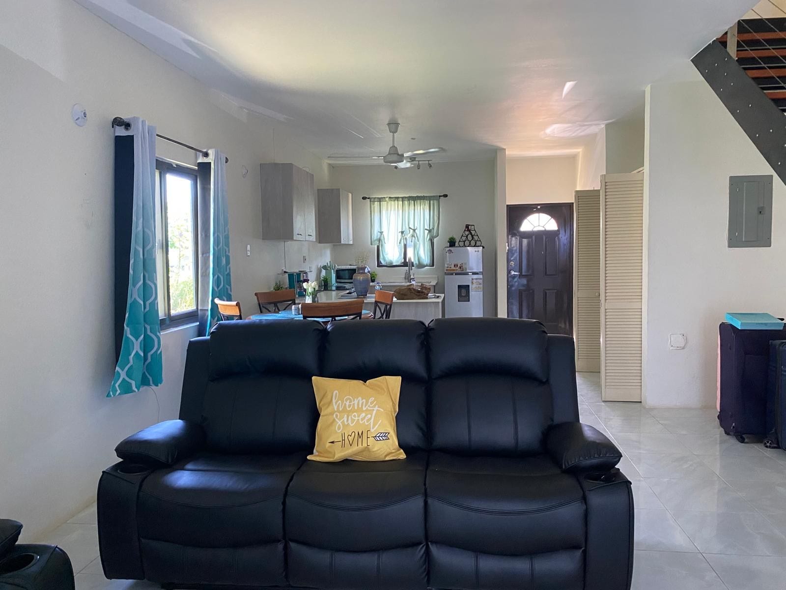 A living room with a black sofa, a yellow pillow, and a dining area in the background.