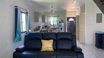 A living room with a black sofa, a yellow pillow, and a dining area in the background.