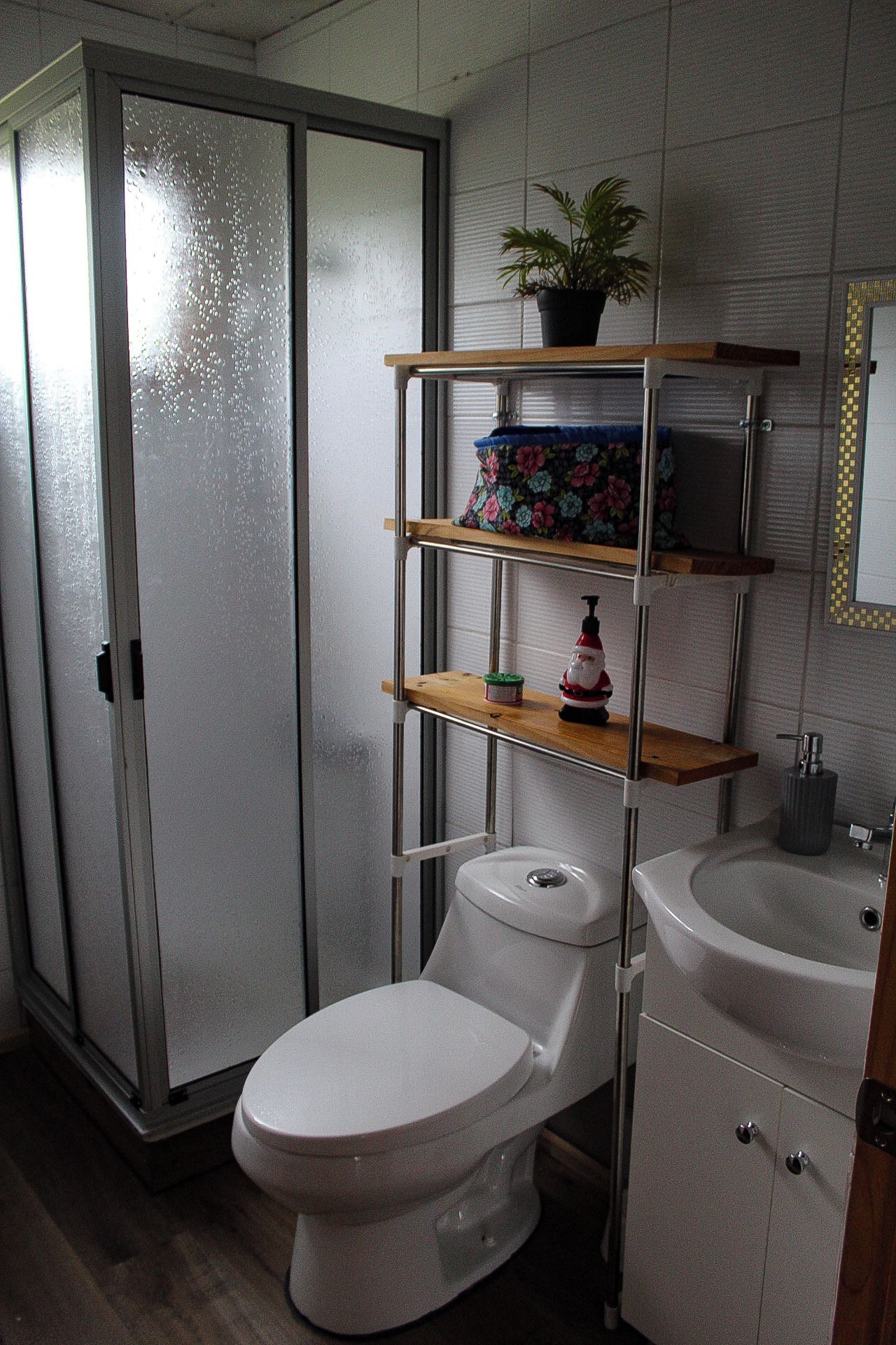 Et badeværelse med toilet, vask og et hyldesæt med en potteplante.