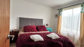 A bedroom with a bed, a nightstand, a window with curtains, and a door.