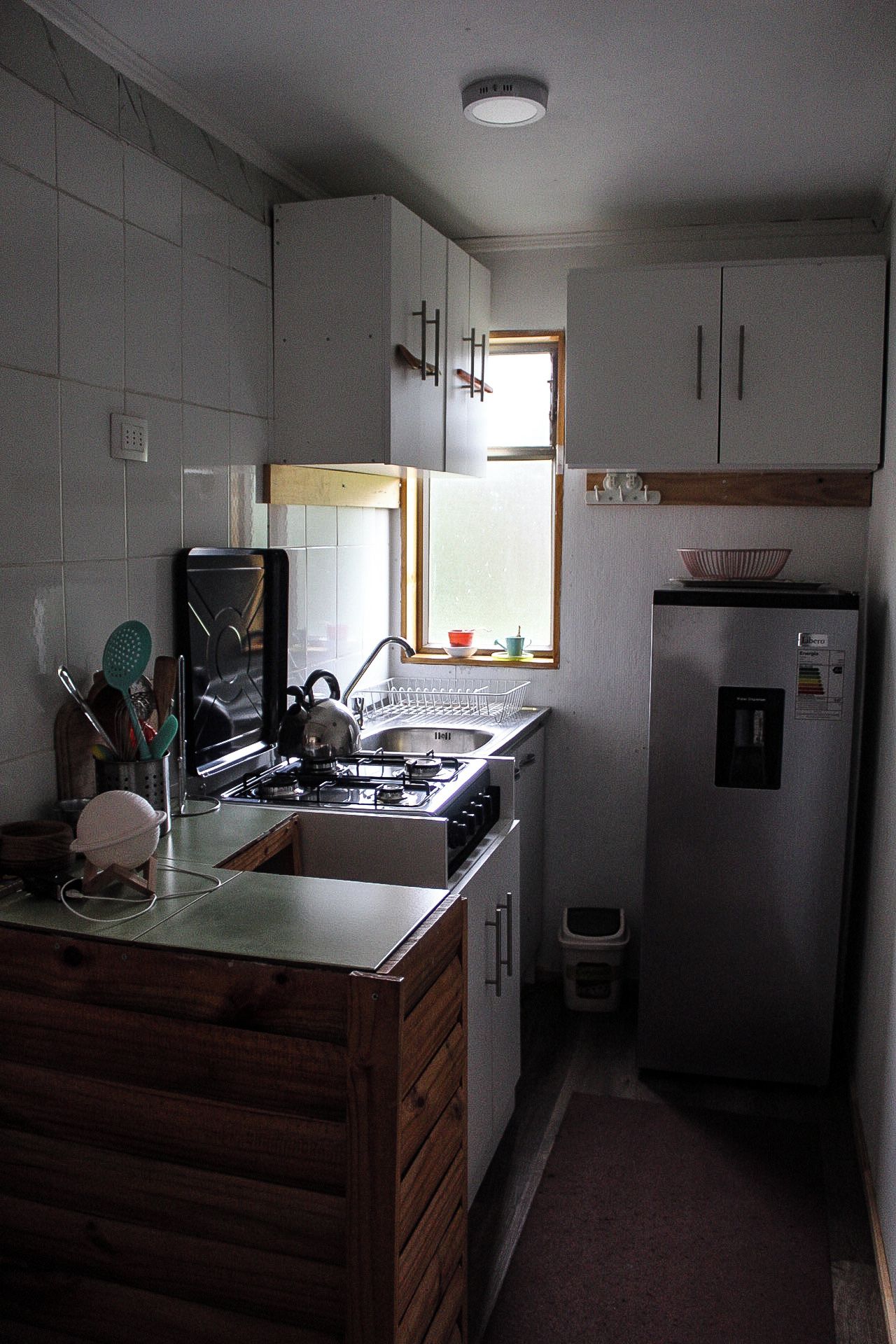 A compact kitchen with a gas stove, a sink, and a refrigerator. There is a window above the sink allowing natural light.