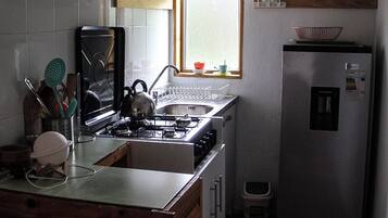 A compact kitchen with a gas stove, a sink, and a refrigerator. There is a window above the sink allowing natural light.