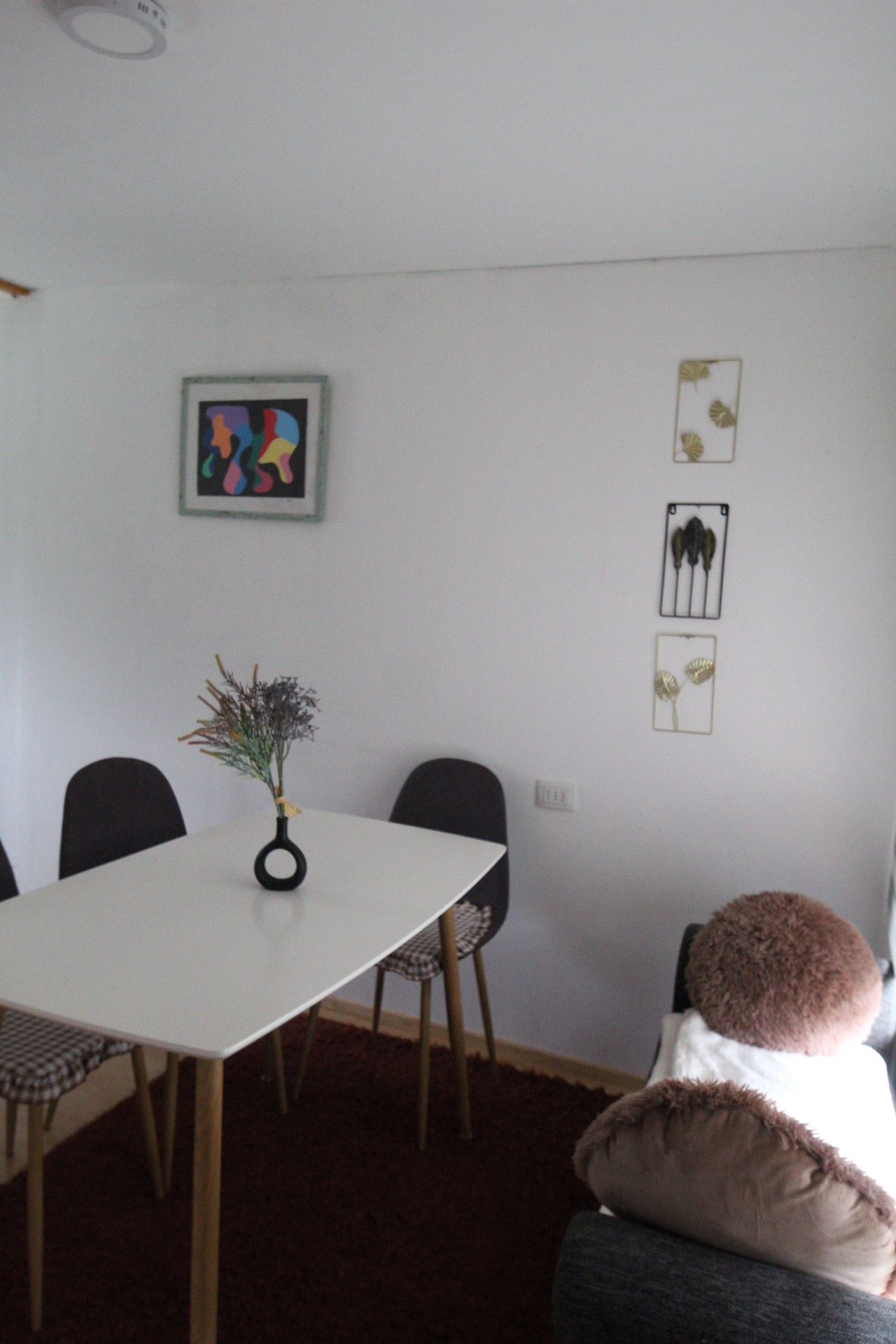 A dining area with a white table, black chairs, and a vase with dried plants.