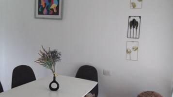 A dining area with a white table, black chairs, and a vase with dried plants.