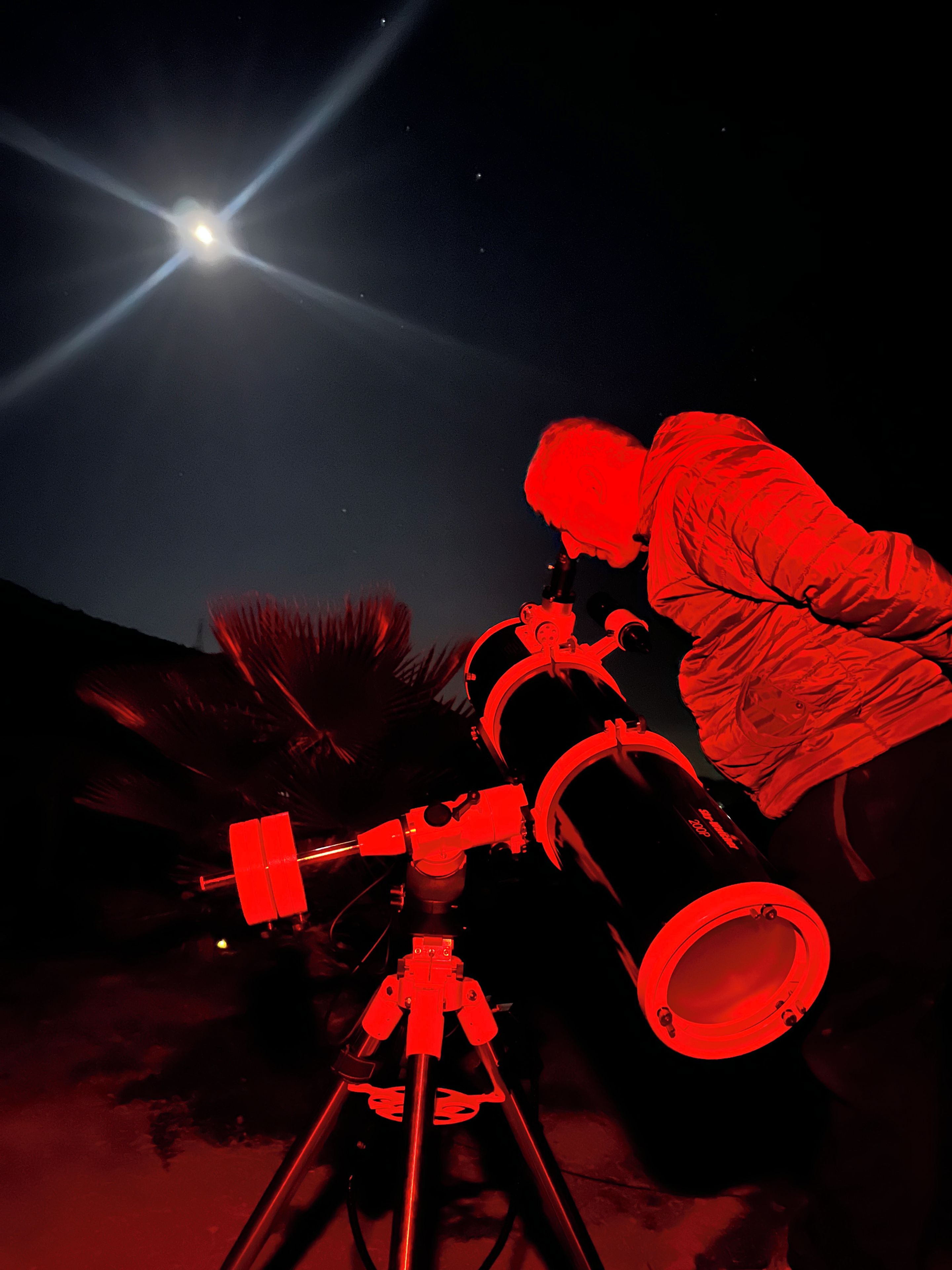 Un télescope, avec une personne qui l’utilise, sur fond de ciel nocturne illuminé par une lune brillante.