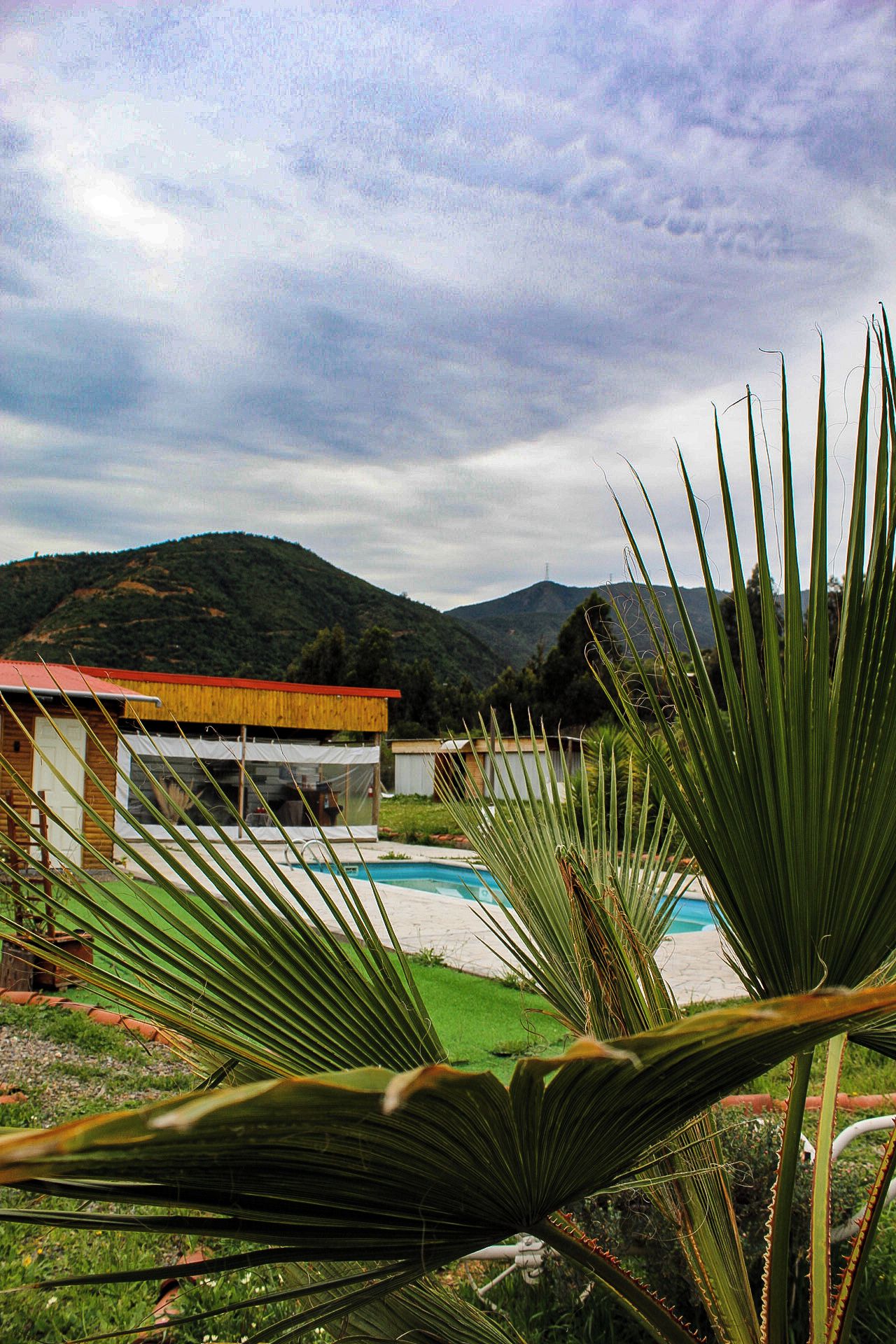 A pool area with a building in the background, surrounded by greenery and hills.