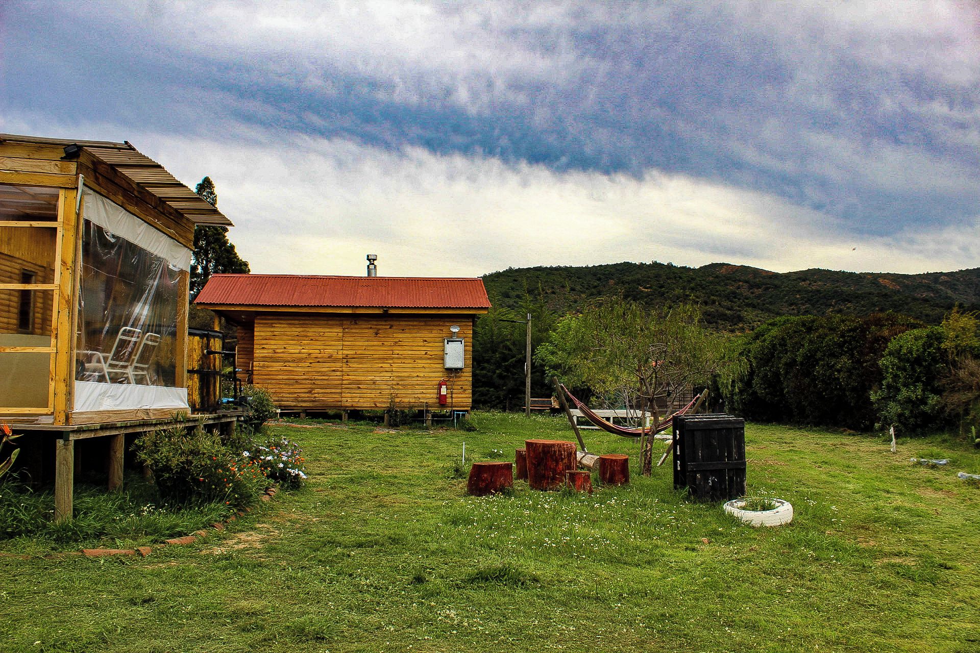 A wooden cabin with a red roof, surrounded by a grassy field and trees.