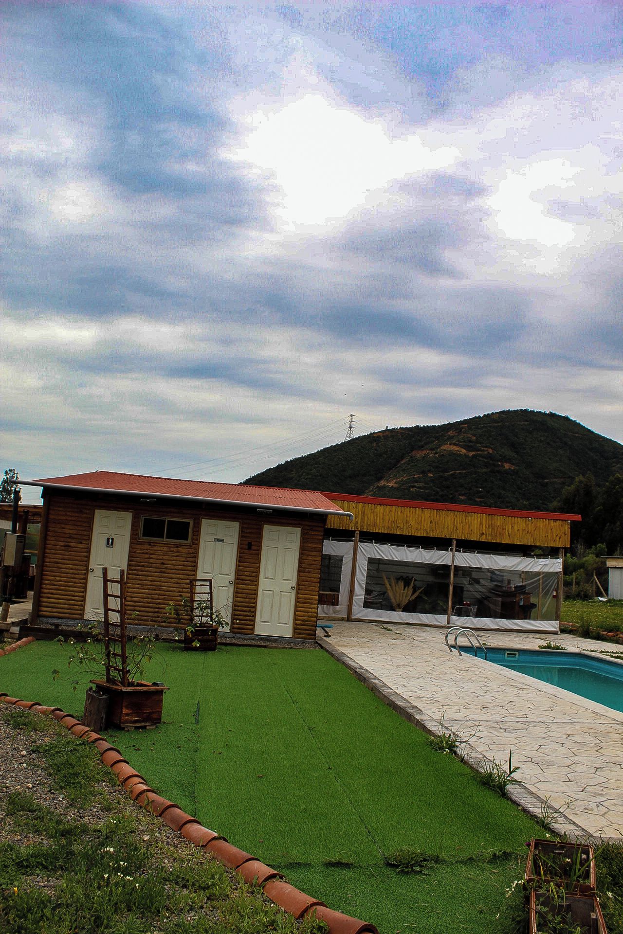 A wooden cabin with a red roof, a covered outdoor area, and a swimming pool.