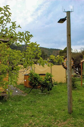 A wooden utility pole with a dartboard, surrounded by greenery and a yellow fence.