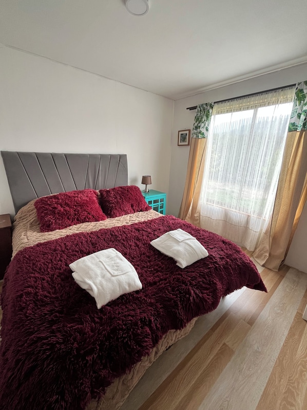 A bedroom with a large bed, a nightstand, a lamp, and a window with curtains.