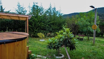 A wooden deck with a circular seating area, surrounded by lush greenery and a small tree.
