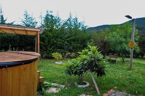 Une terrasse en bois dotée d’un espace de détente circulaire, entourée d’une végétation luxuriante et d’un petit arbre.