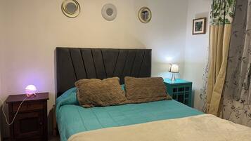 A bedroom with a bed, a nightstand, a lamp, and a wall with three mirrors.