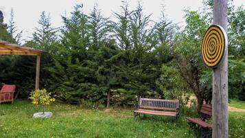 A wooden bench, a target post, and a gazebo in a grassy area with trees.
