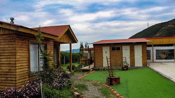 A wooden cabin with a porch, a small garden with flowers, and a clear sky.