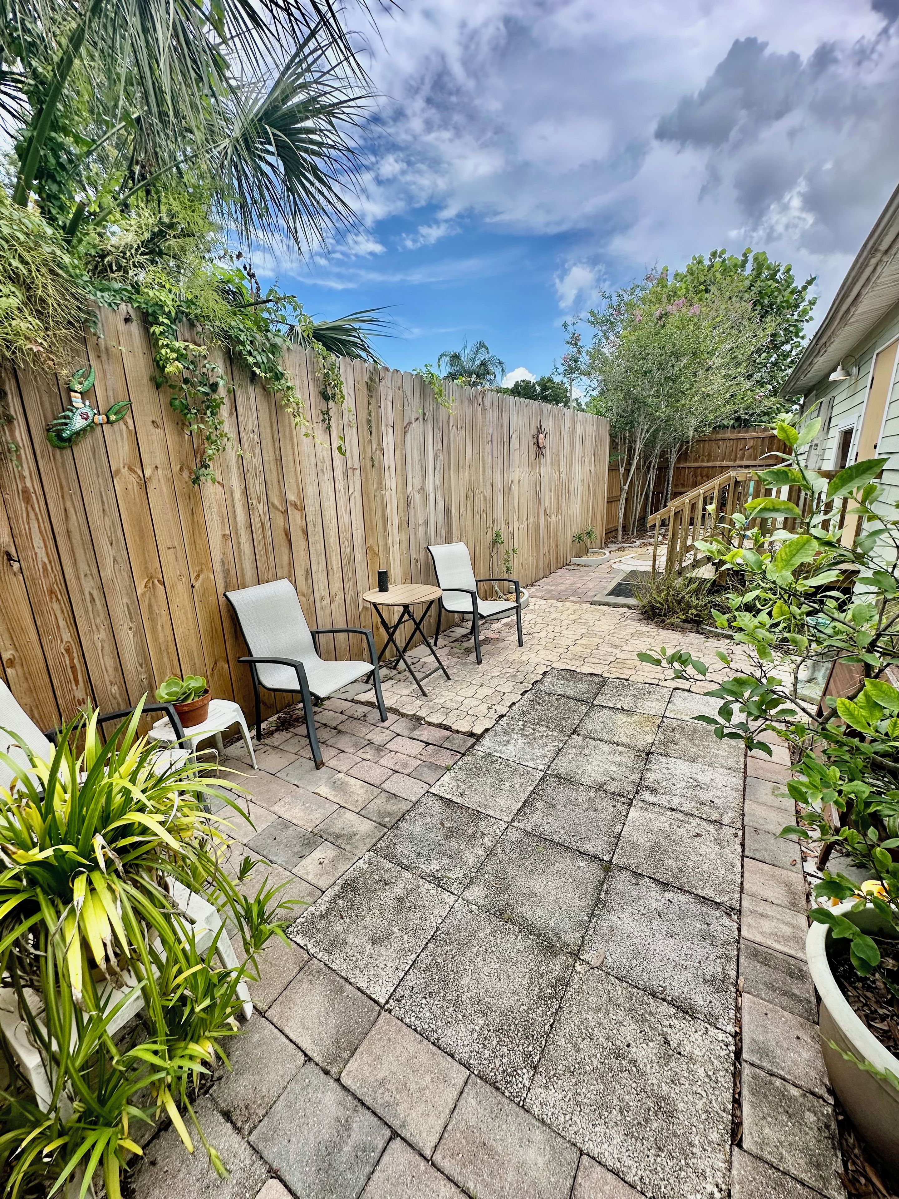 A patio with a wooden fence, outdoor seating, and potted plants.