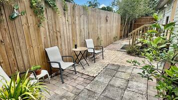 A patio with a wooden fence, outdoor seating, and potted plants.