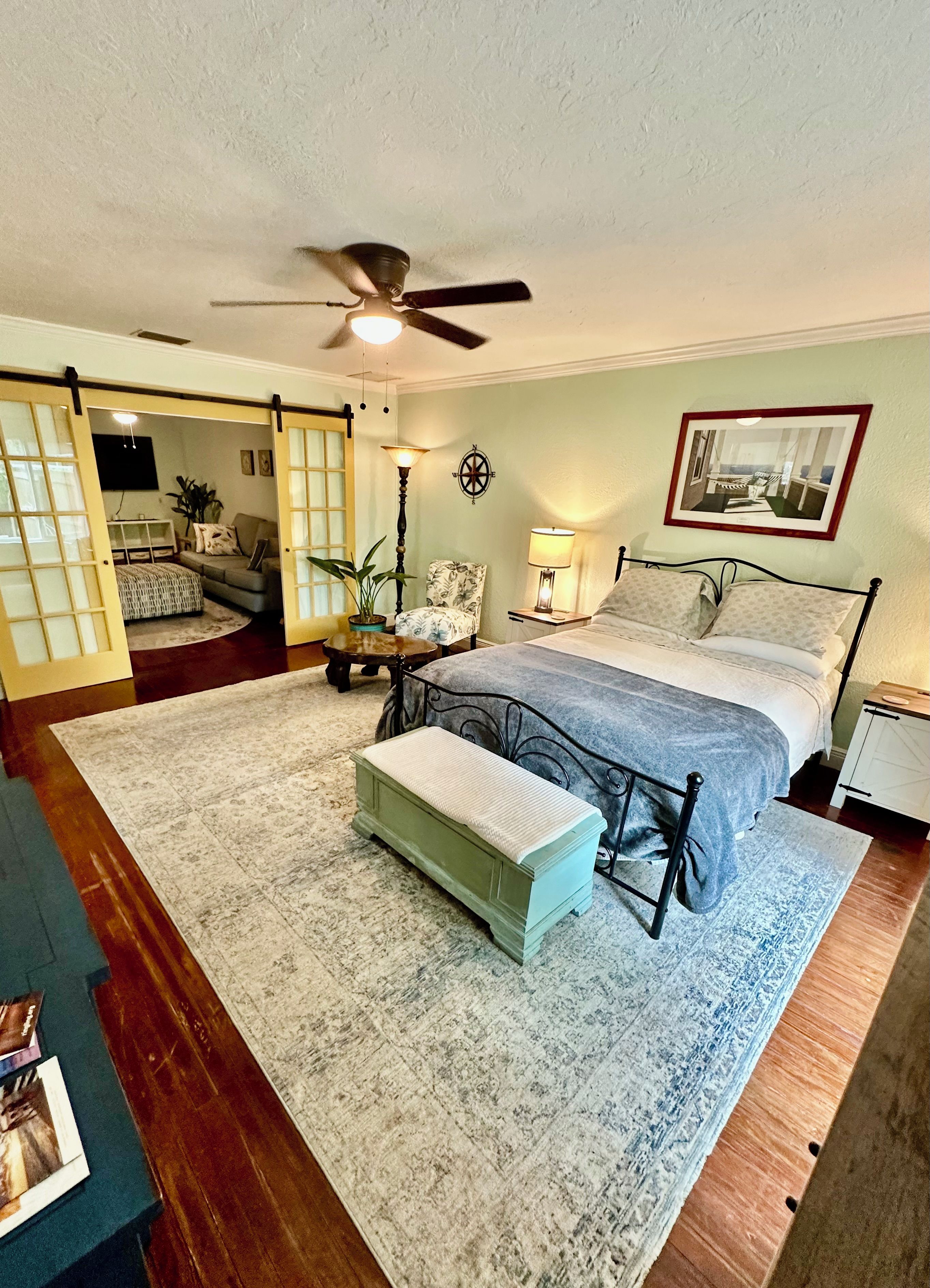 A bedroom with a bed, bedside tables, a ceiling fan, a wall-mounted lamp, and a framed picture.