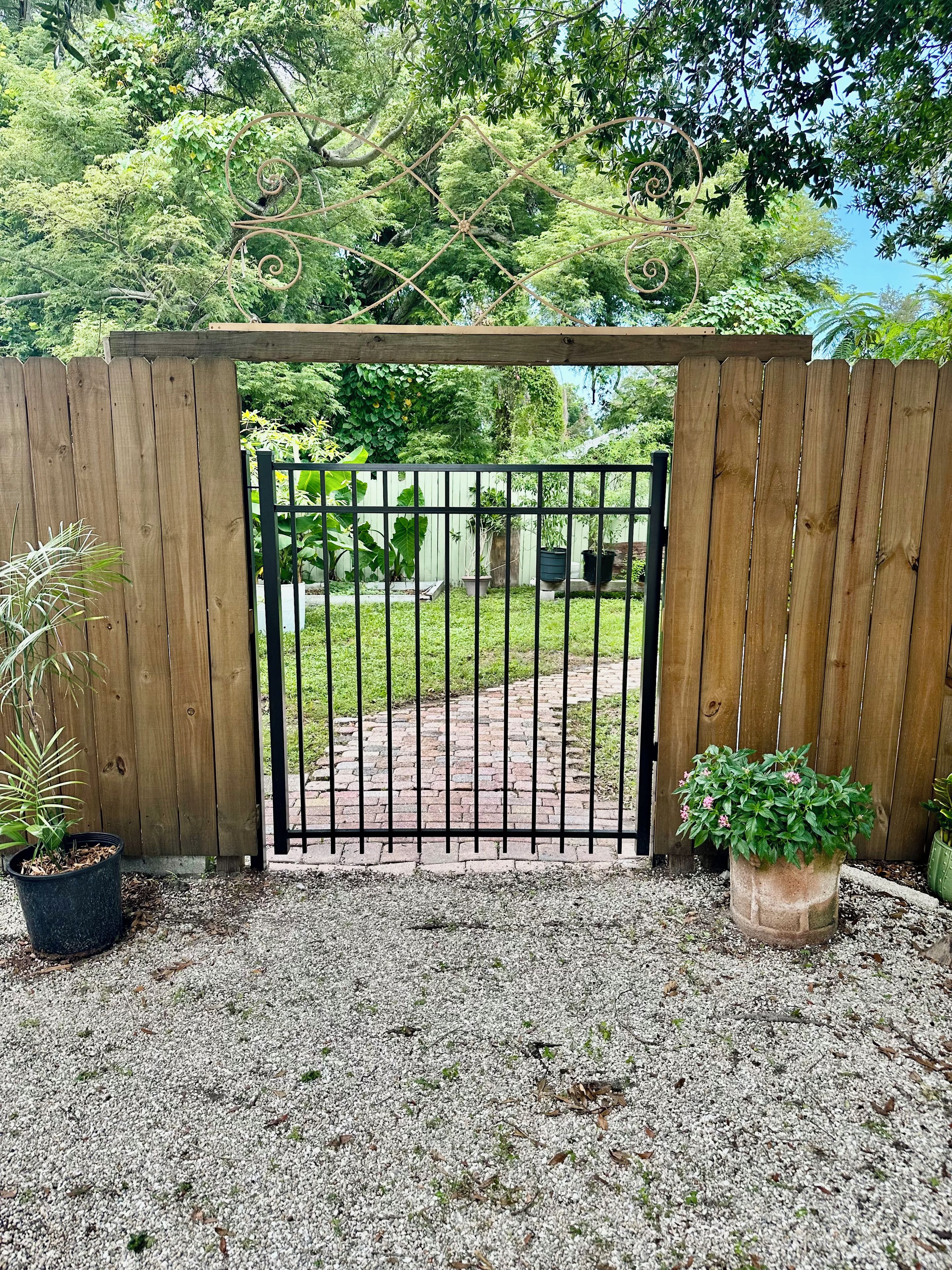 A wooden gate with a metal gate, gravel ground, and potted plants.