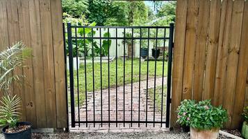 A wooden gate with a metal gate, gravel ground, and potted plants.