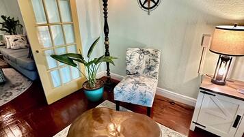 A room with a wooden bench, a potted plant, a chair with floral upholstery, a lamp, and a compass wall decoration.