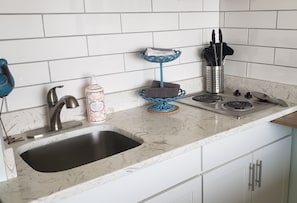 Una cocina con un lavabo, grifo, jabón para lavar platos, un toallero azul y un portacuchillos.