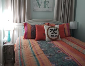 A bedroom with a bed, pillows, a nightstand, a lamp, and a wall with a sign. - END Condo directly on the Beach with unobstructed views of the ocean (Corpus Christi)