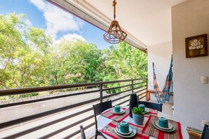 Ein Balkon mit Esstisch, der auf eine Straße und Bäume blickt.