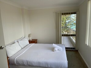 Ett hotellrum med en säng, ett nattduksbord, ett fönster med utsikt över en balkong och en dörr.