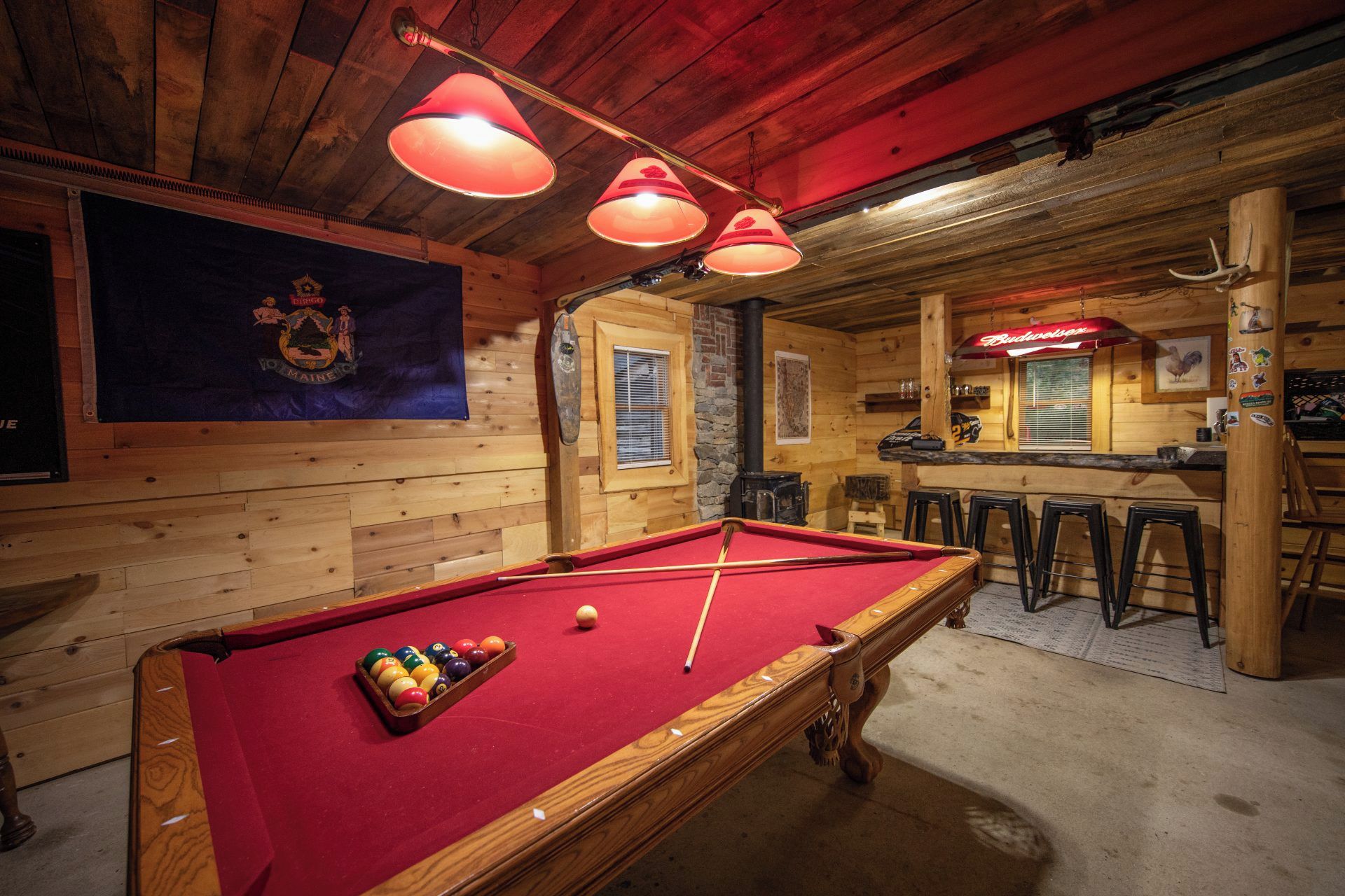 Une table de billard avec des billes, un coin bar avec des tabourets et un intérieur en bois.