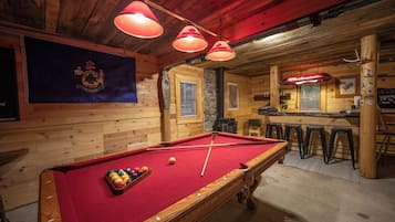 A pool table with balls, a bar area with stools, and a wooden interior.