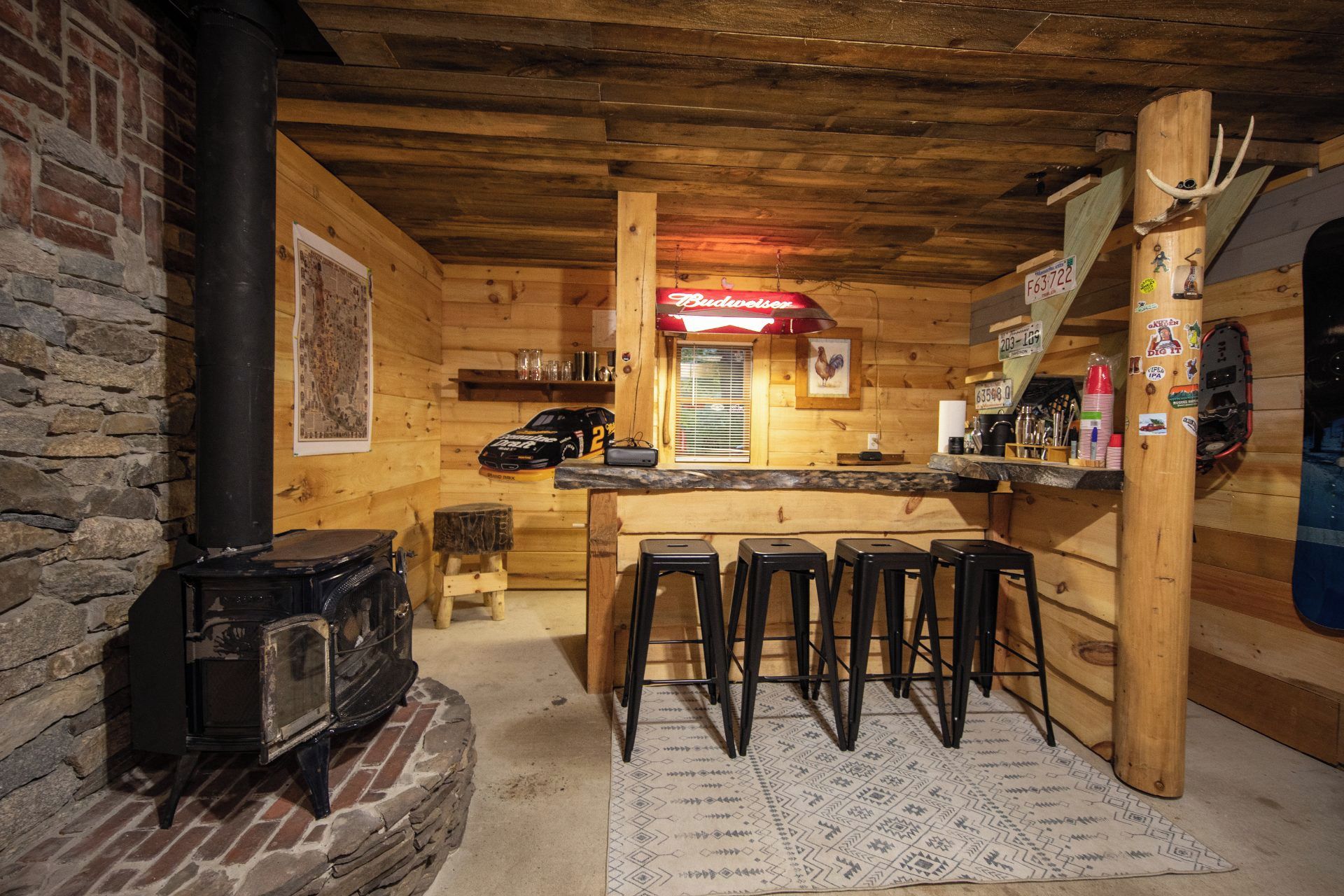 A rustic wooden interior with a bar area, stools, a fireplace, and a map on the wall.
