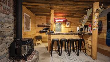 A rustic wooden interior with a bar area, stools, a fireplace, and a map on the wall.