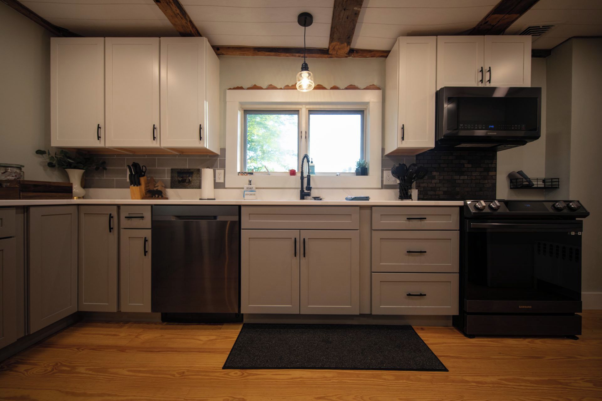 A kitchen with white cabinets, a stainless steel dishwasher, a black oven, and a window above the sink.