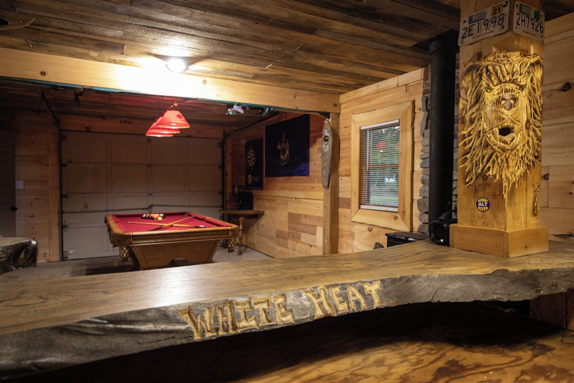A wooden interior with a pool table, a wooden pillar with carvings, and a sign indicating 'Sunday Alt River.'