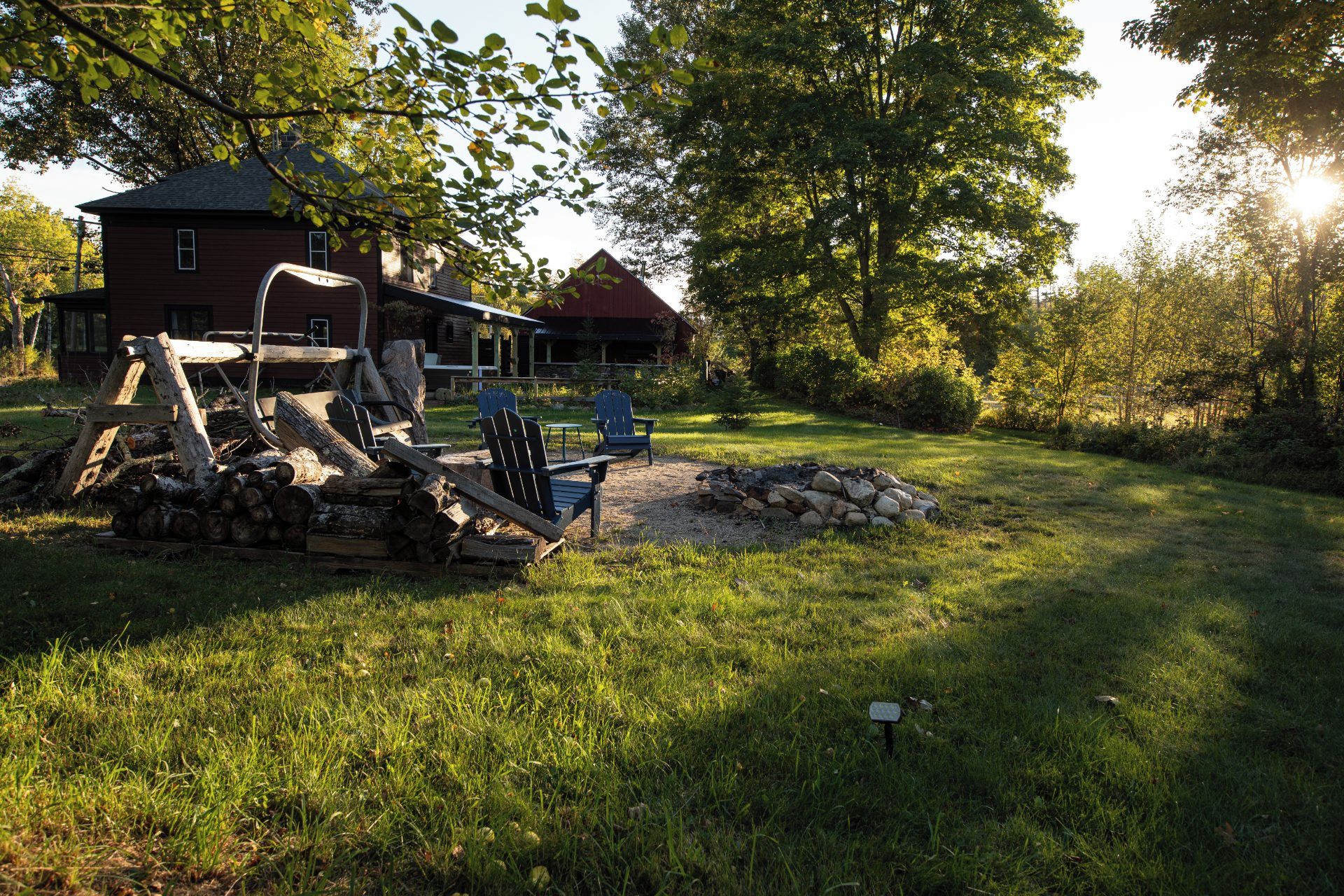 A rustic cabin with a deck, outdoor seating, and a fire pit in a wooded area.