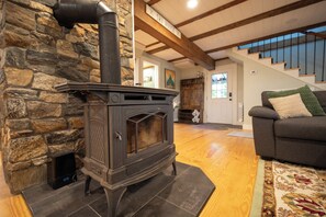 A stone wall with a wood-burning stove, a staircase, and a living room with a sofa. - Farmhouse Escape w/Hot Tub, EV Charger, Ski Bar - 10 mins to Sunday River (Rumford)
