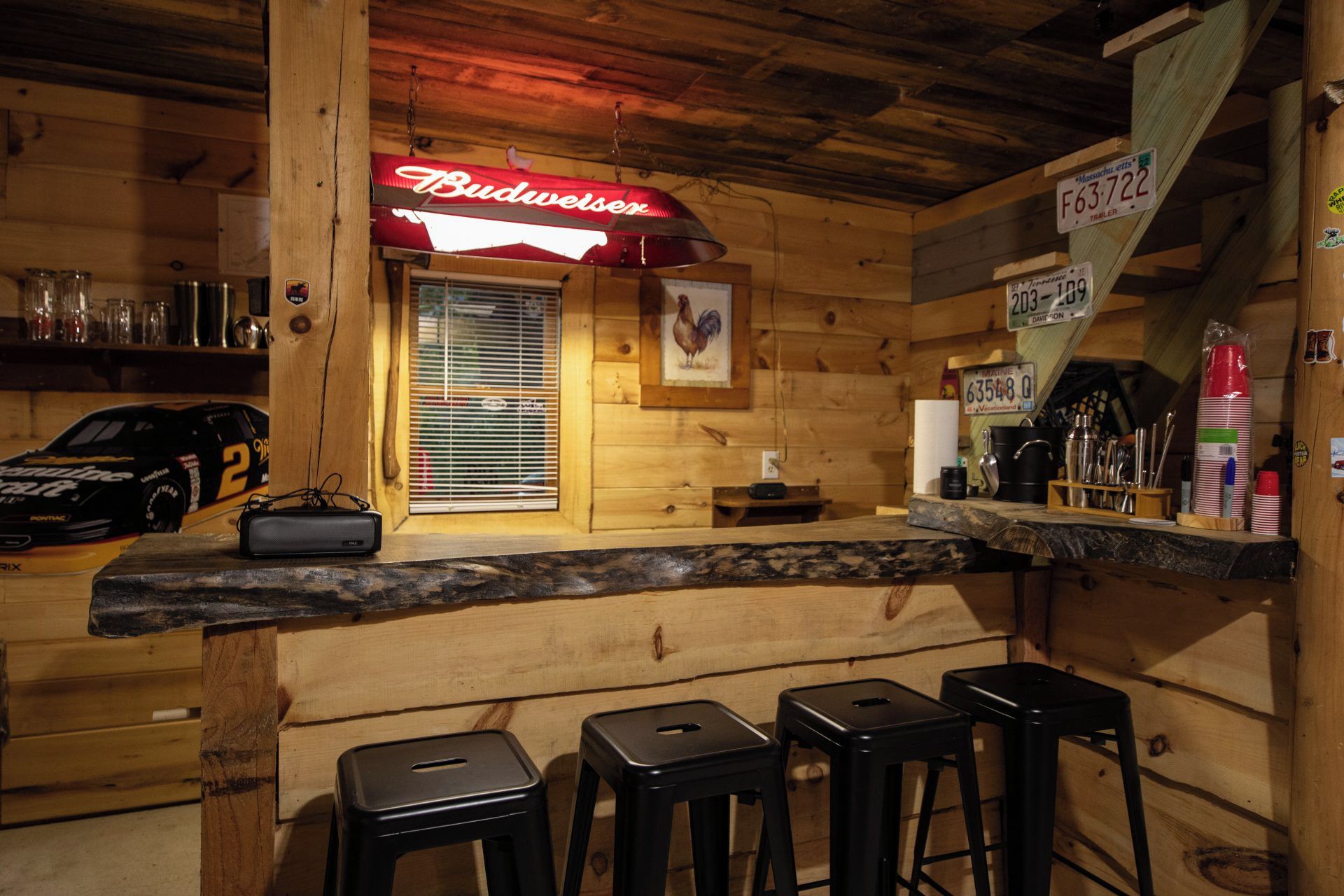 Een barruimte met een Budweiser bord, houten wanden, een model raceauto en barstoelen.