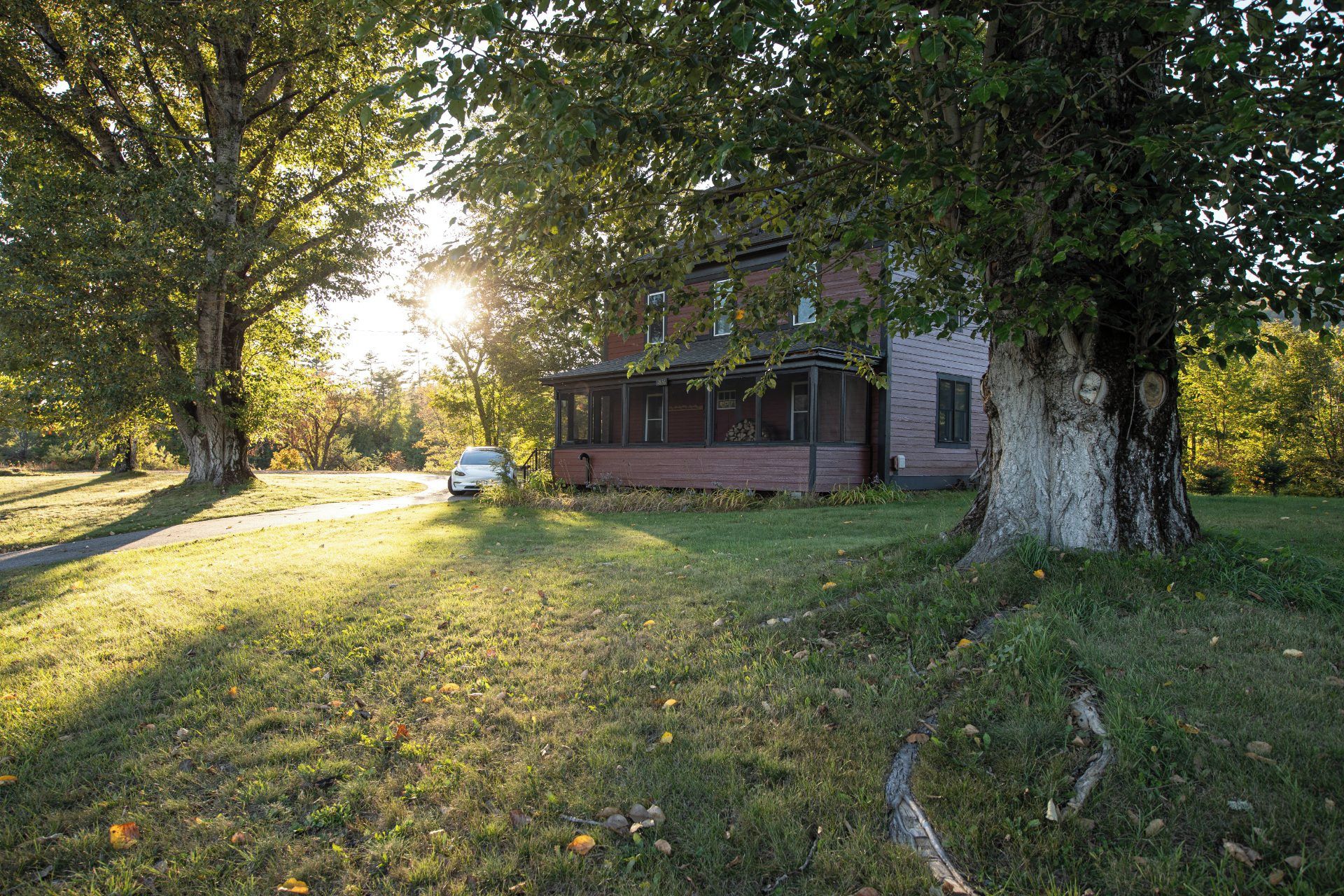 A house with a porch, surrounded by trees and a car parked in the driveway.