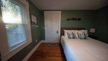 A bedroom with a bed, a door, a window with blinds, and a wall decoration.