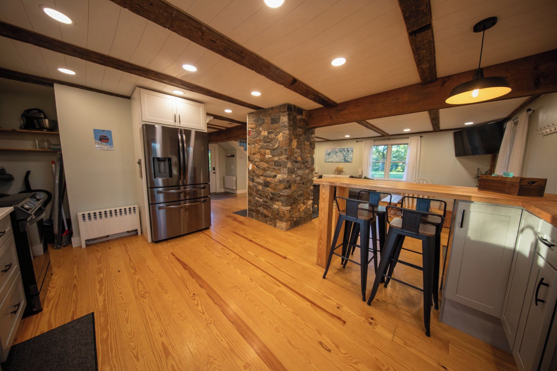 A kitchen with a stone pillar, wooden bar stools, and a stainless steel refrigerator.
