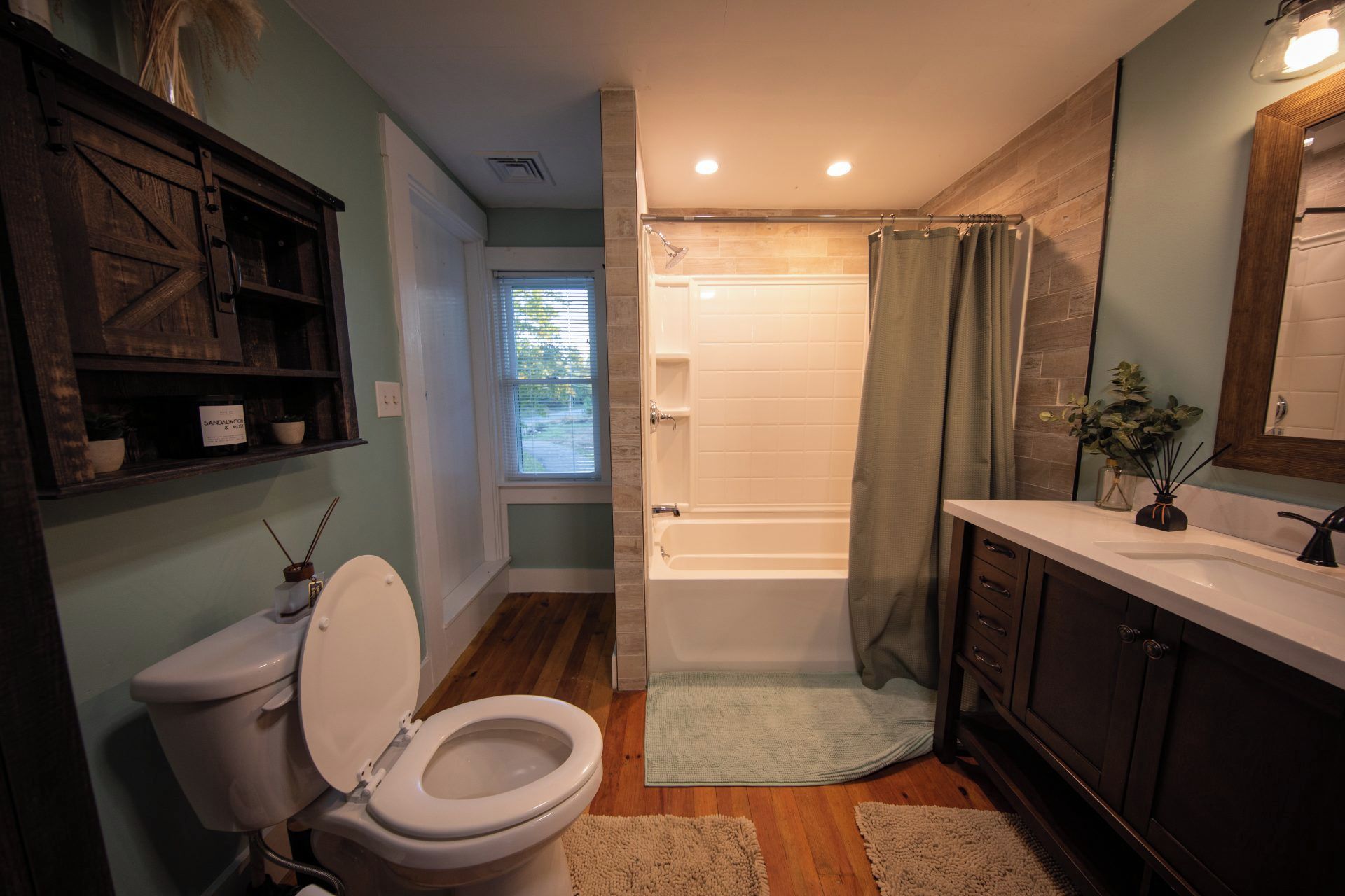 A bathroom with a toilet, bathtub, shower, vanity, and a window.