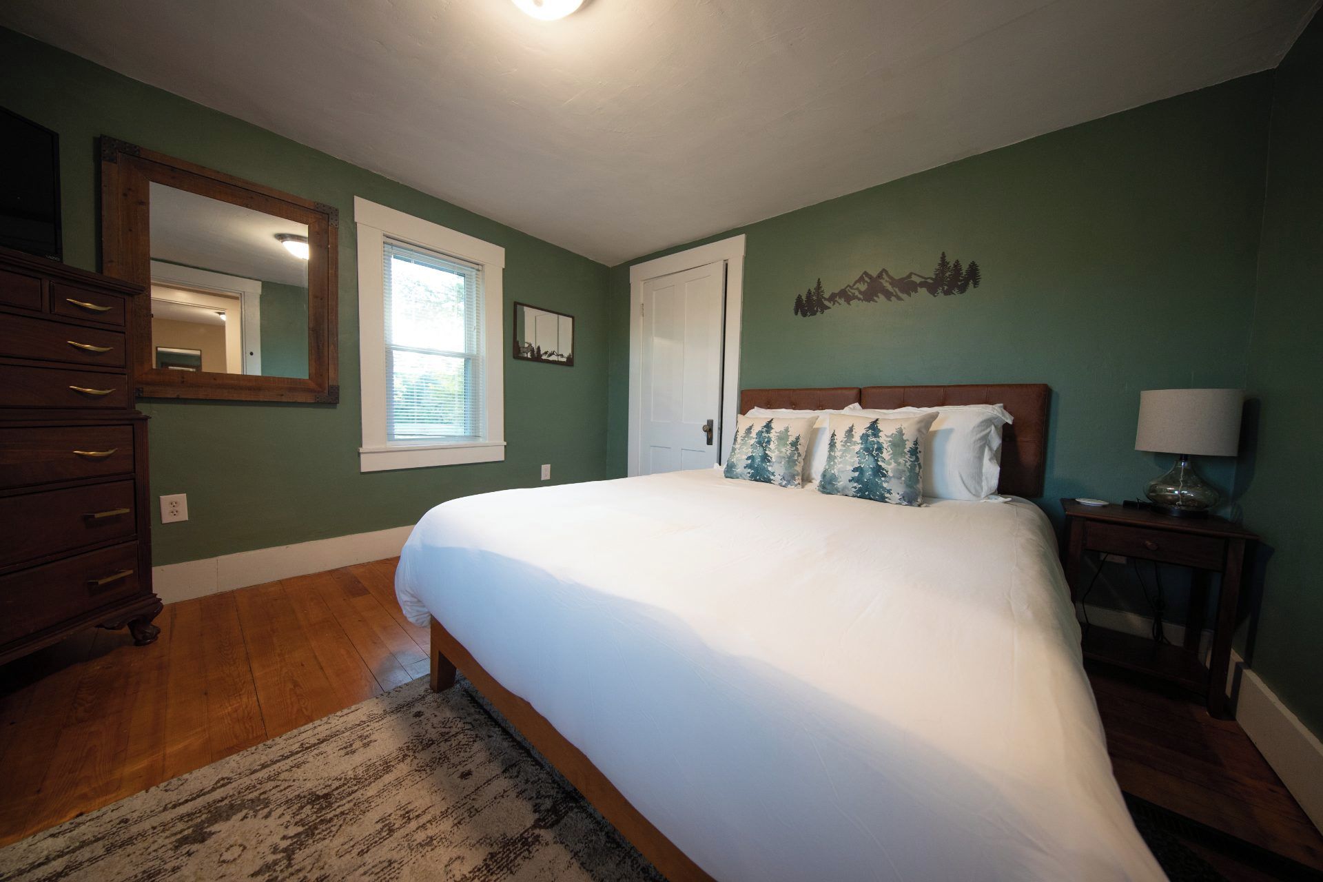 A bedroom with a large bed, a dresser, a nightstand, a lamp, and a mirror.